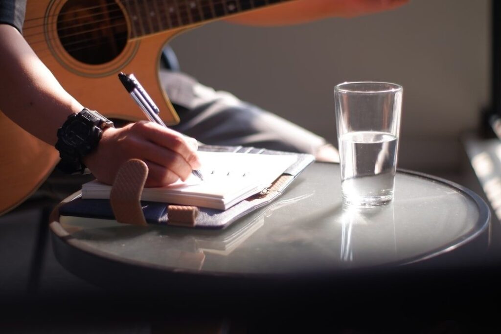 Musiker skriver i en notatbok ved et bord med gitar og vann