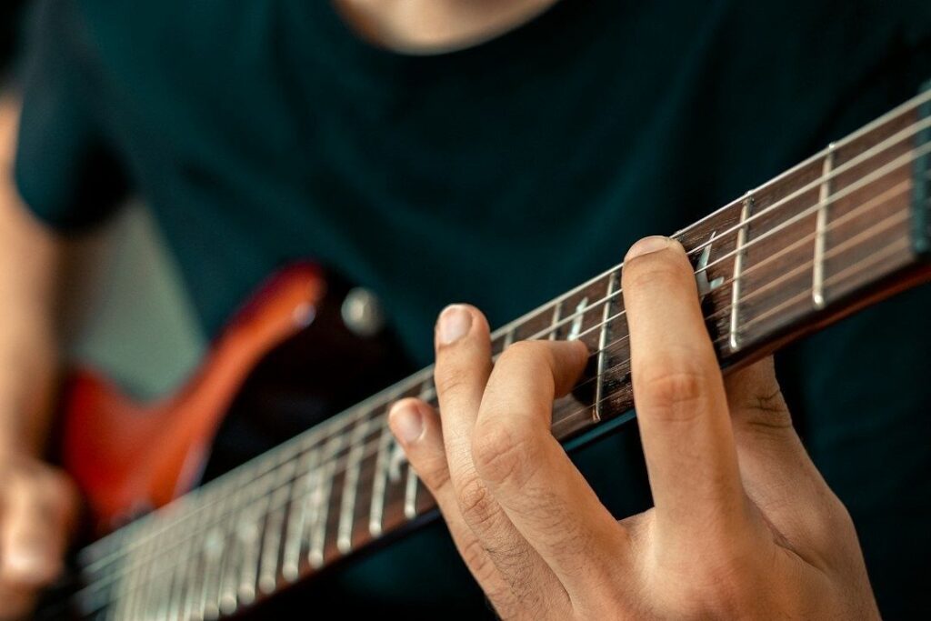 Nærbilde av hånd som spiller gitar med fingrene på gripebrettet